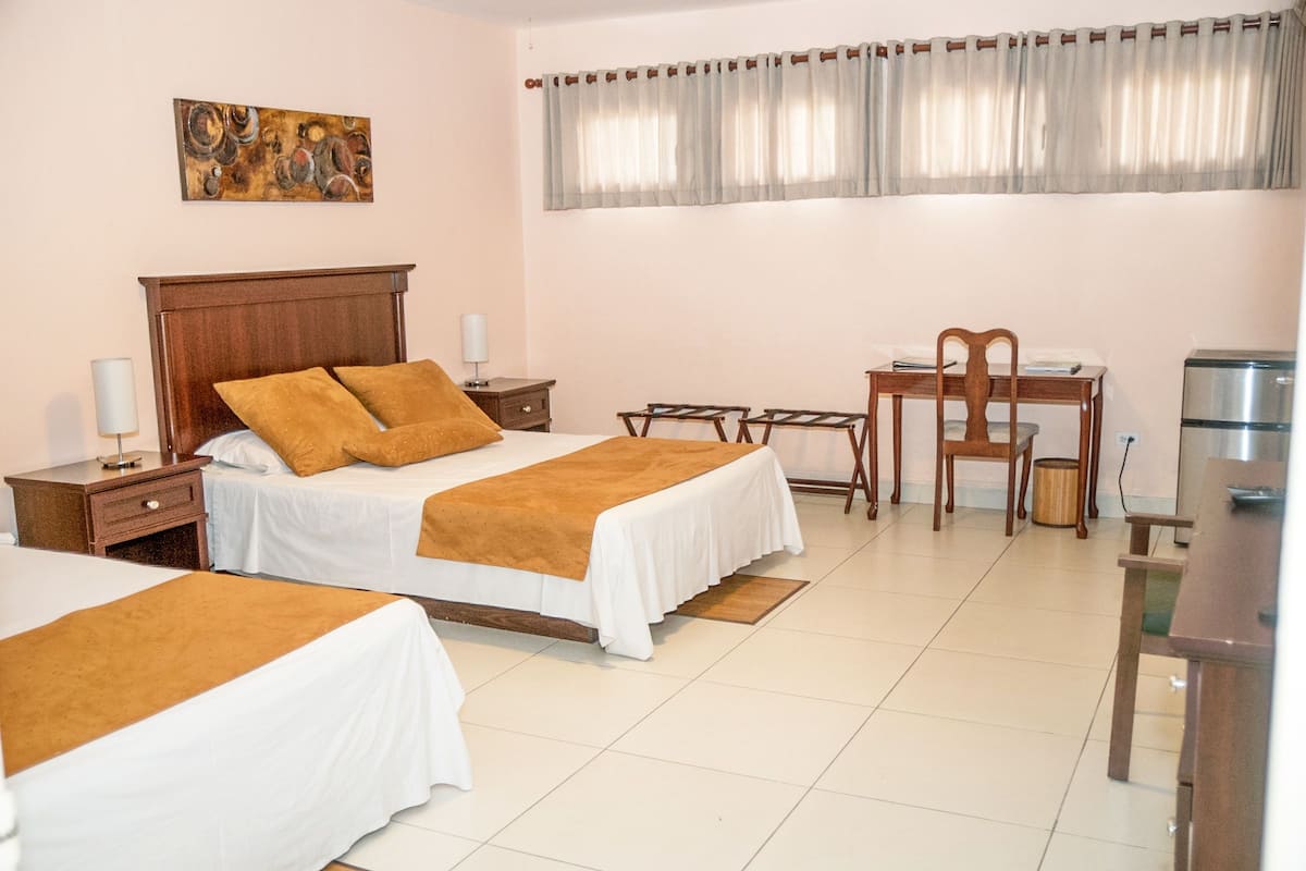 A hotel room with two beds, a desk, a chair, a lamp, and a painting on the wall.
