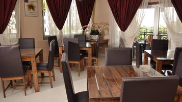 A dining area with wooden tables and black chairs, red curtains, and a view of greenery outside.