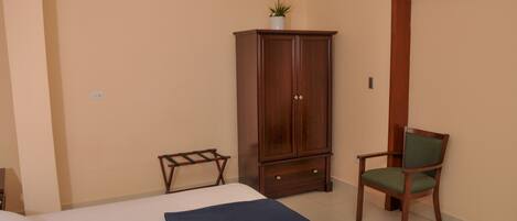 Un dormitorio con una cama, un armario de madera, una silla y una planta en maceta.