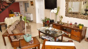 A living room with a sofa, coffee table, and TV. There is a staircase in the background. - Allamanda Hotel (Petionville)