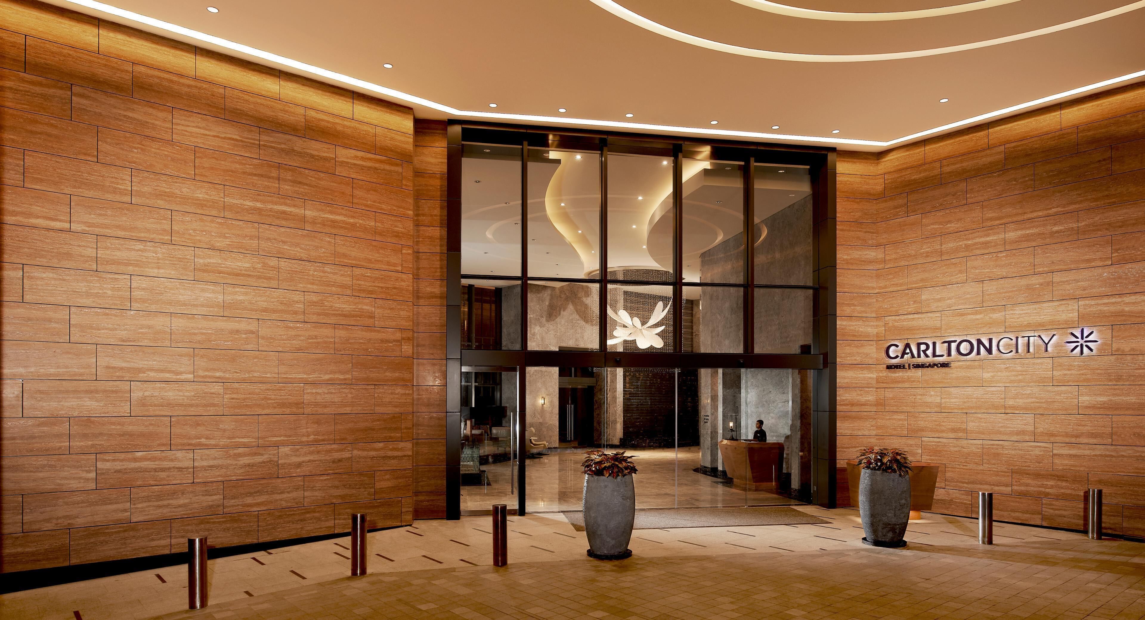 A hotel lobby with a wooden wall, a reception desk, and a large glass entrance.