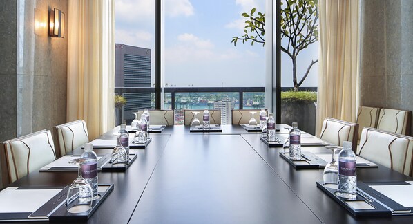 A conference room with a long table, chairs, water bottles, and a view of a cityscape.