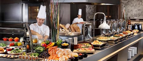 Disposición de bufé con diversas opciones de comida y un cocinero preparando alimentos.