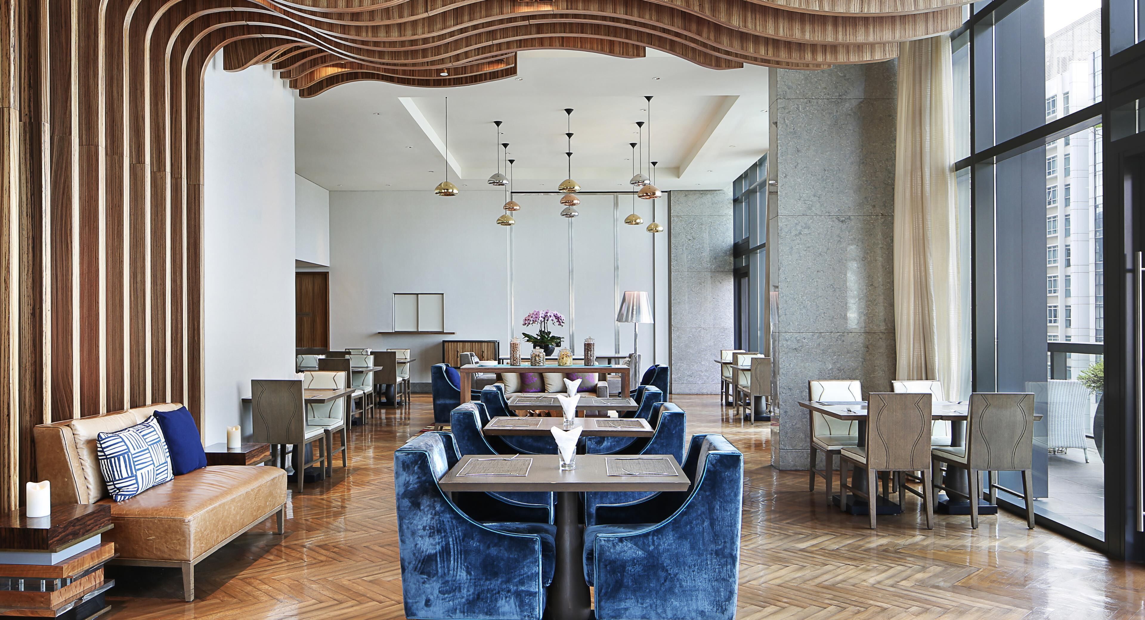 A modern dining area with wooden paneling, a herringbone floor, and a mix of seating options including tables and sofas.