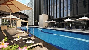 A modern hotel pool area with lounge chairs and umbrellas, surrounded by tall buildings. - Carlton City Hotel Singapore (Singapore)