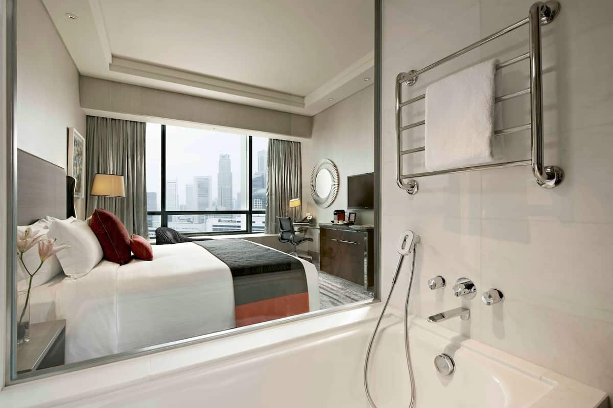 A hotel room with a large bed, a bathroom with a bathtub, a desk, and a view of the city through the window.