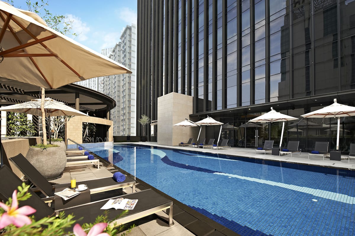 A rooftop pool area with lounge chairs and umbrellas, surrounded by tall buildings.