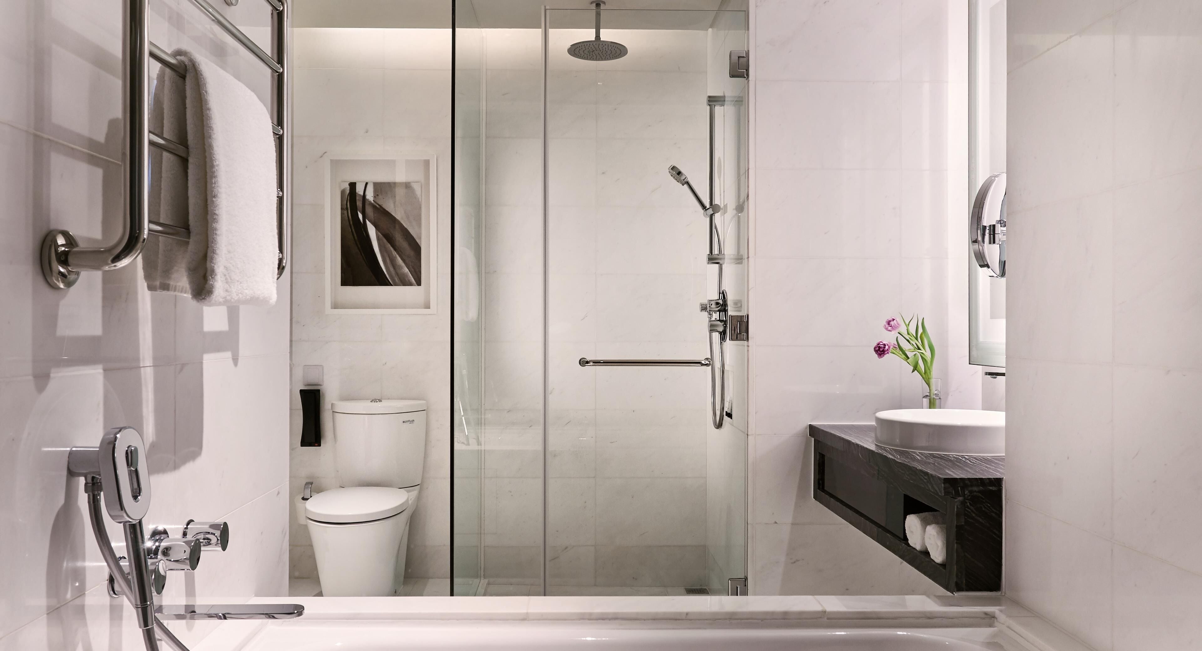 Une salle de bain moderne dotée d’une douche à parois de verre, de toilettes, d’un lavabo avec un plan de travail en marbre et d’un porte-serviettes.