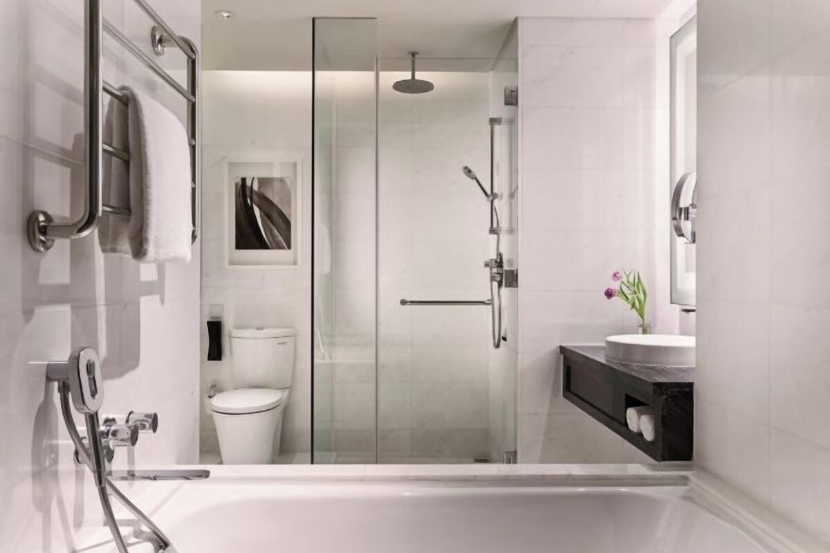 Un baño moderno con ducha de vidrio, inodoro blanco y tocador con lavabo y espejo.