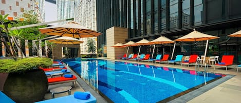 A swimming pool with lounge chairs and umbrellas, surrounded by tall buildings.