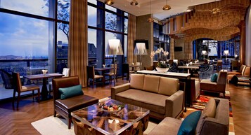 A modern hotel lobby with a large seating area, a bar, and a view of the cityscape.