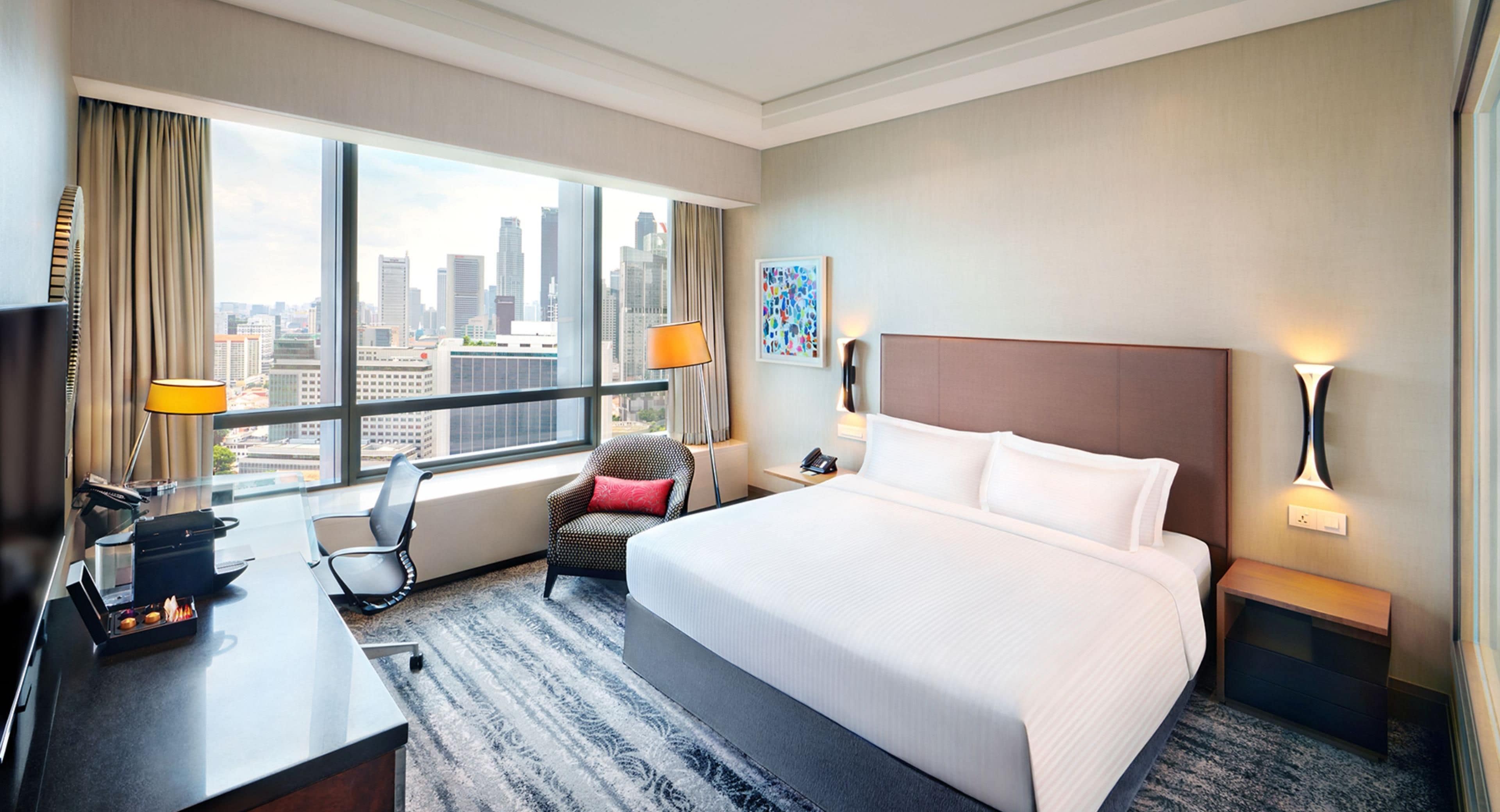 Habitación de hotel con cama, escritorio, silla, vista a la ciudad y ventana con cortinas.