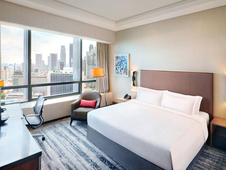 Habitación de hotel con cama, escritorio, silla, vista a la ciudad y ventana con cortinas.