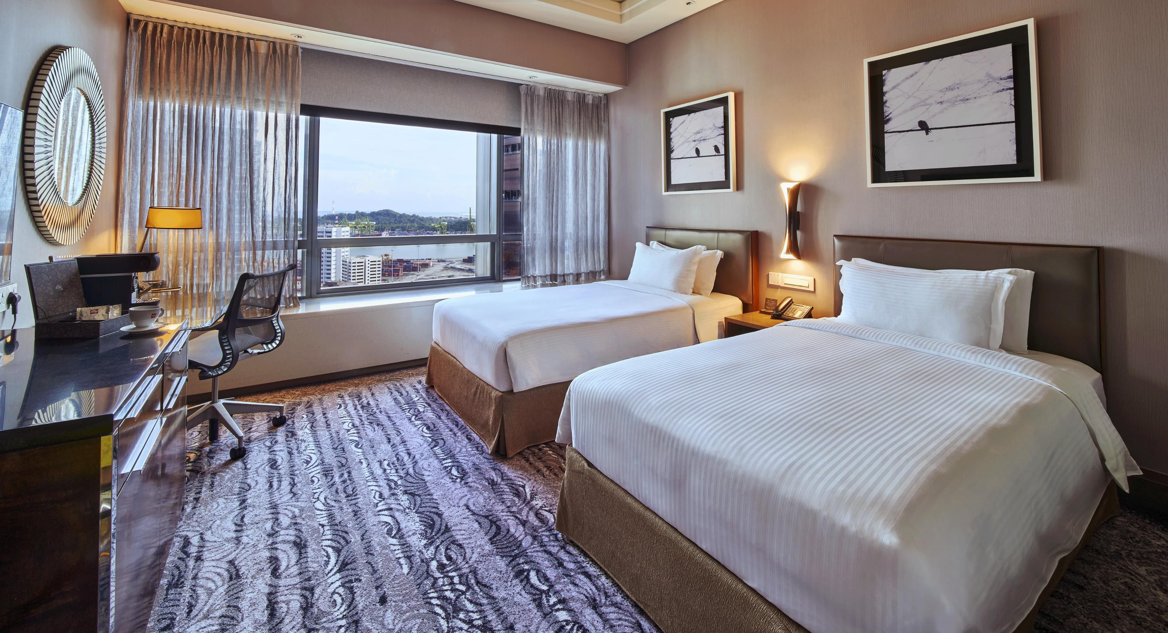 A hotel room with two beds, a desk with a chair, a coffee maker, and a view of buildings through the window.