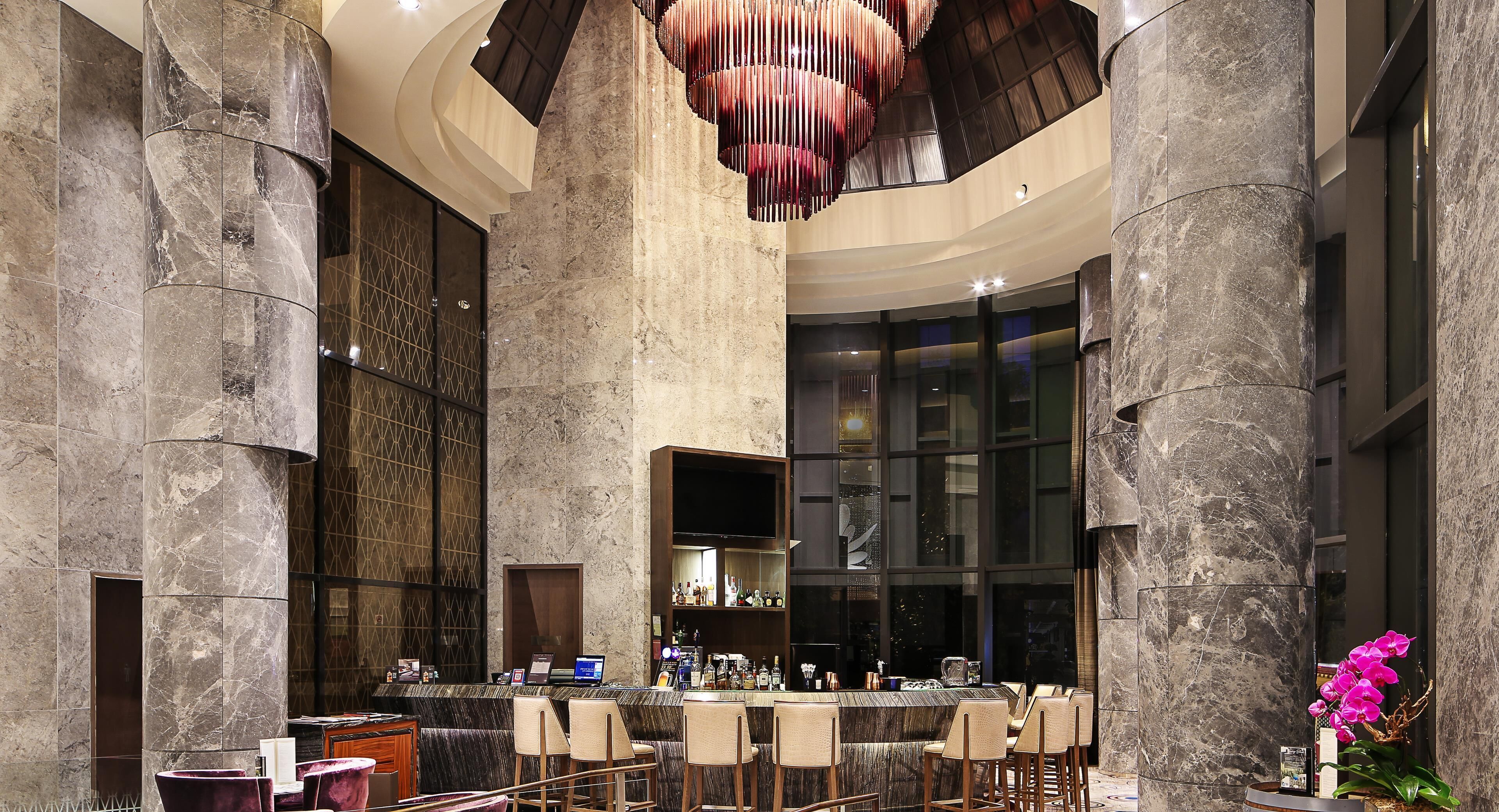 A bar area with marble columns, a modern chandelier, and a bar counter with seating.