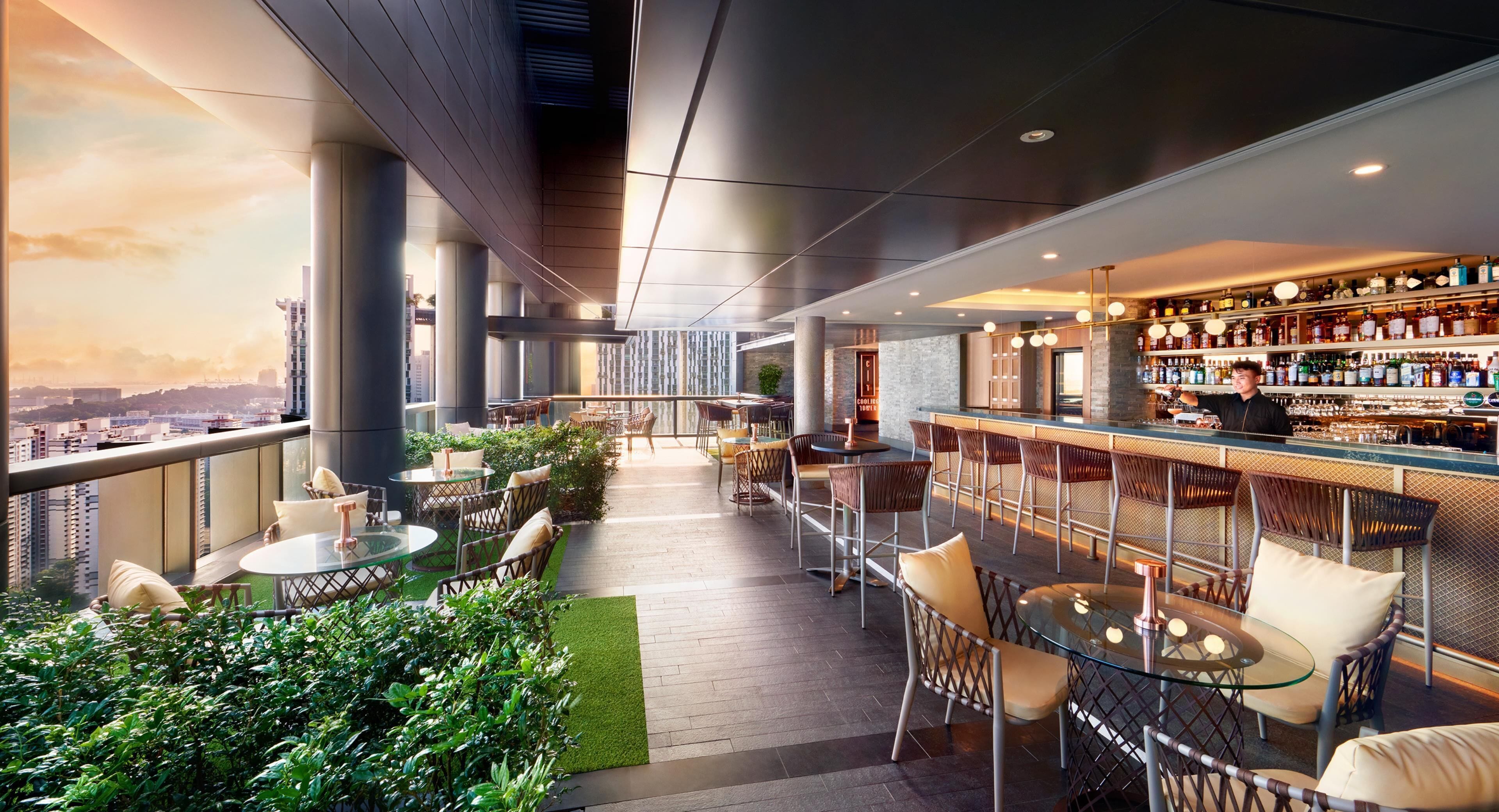 A rooftop bar with outdoor seating, a bar counter, and a city view.