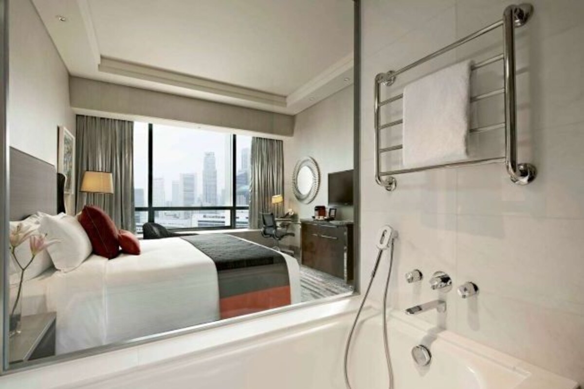 Una habitación de hotel moderna con una cama grande, un baño con bañera, un escritorio y vistas a la ciudad.
