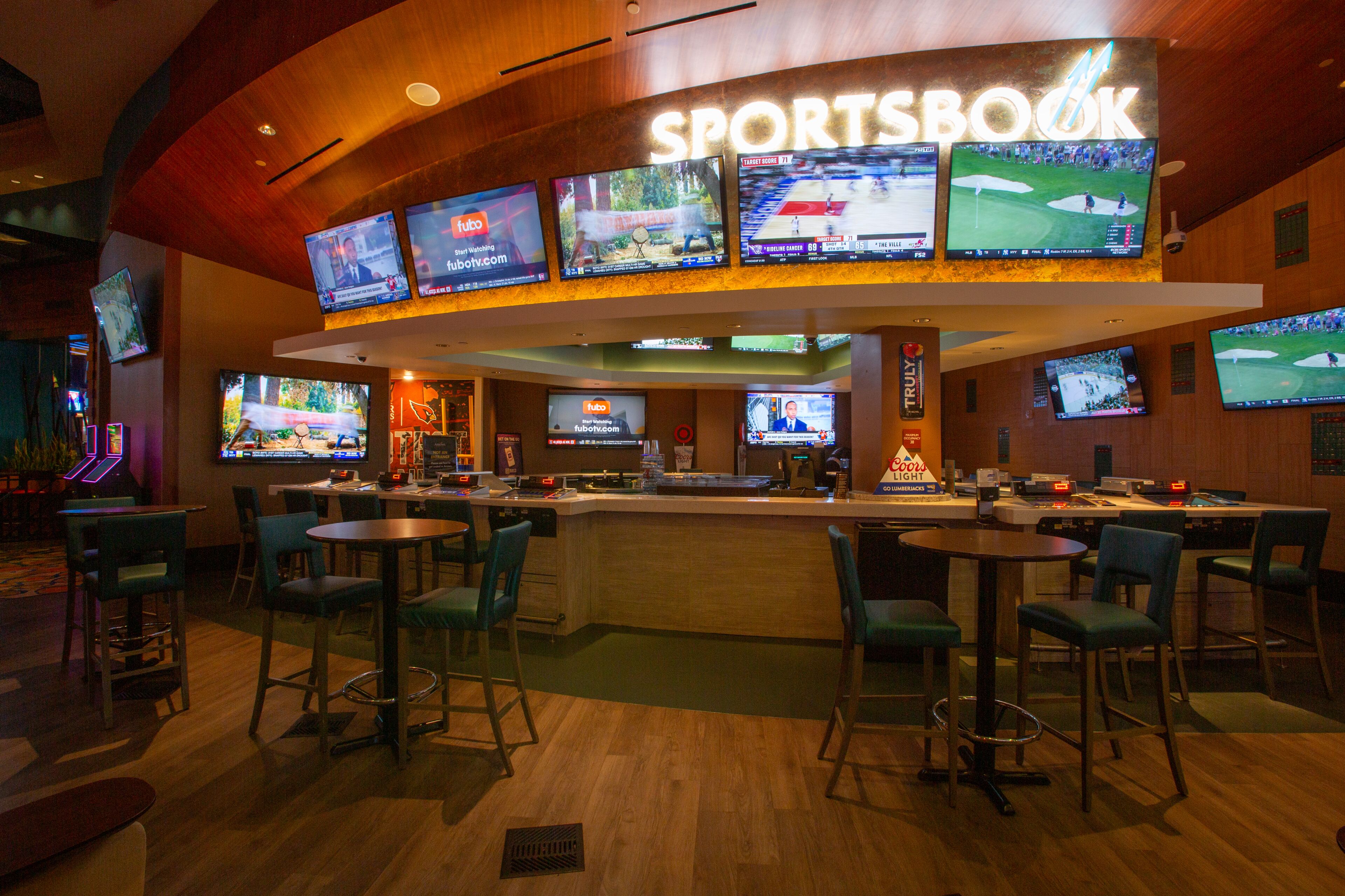 A sports bar with multiple screens displaying various sports events, bar area with stools, and a counter with a menu.