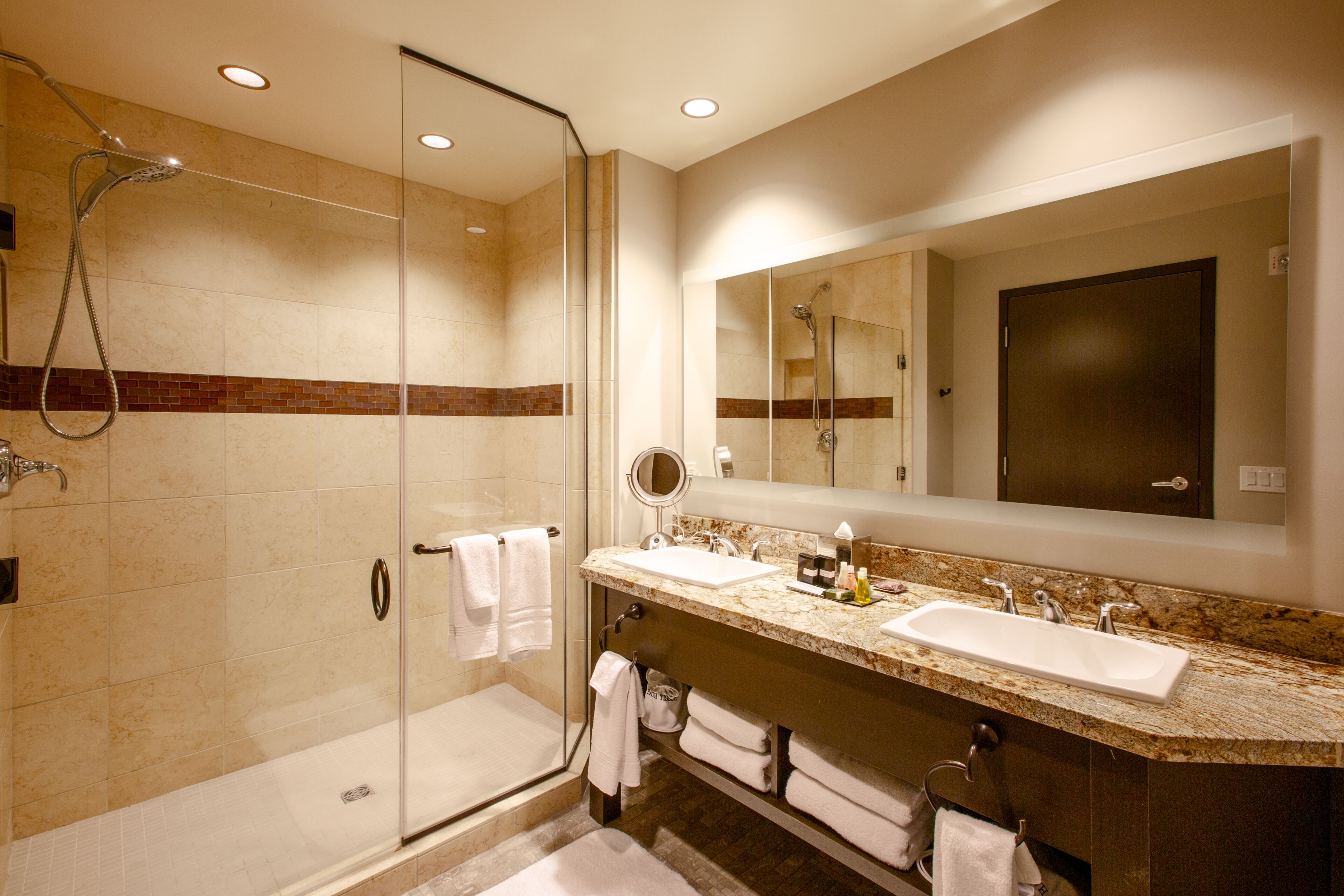 A modern bathroom with a glass-enclosed shower, dual sinks, and a large mirror.