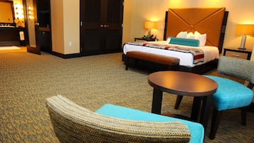 A hotel room with a bed, bedside tables, a round table, and a seating area with a chair and ottoman.