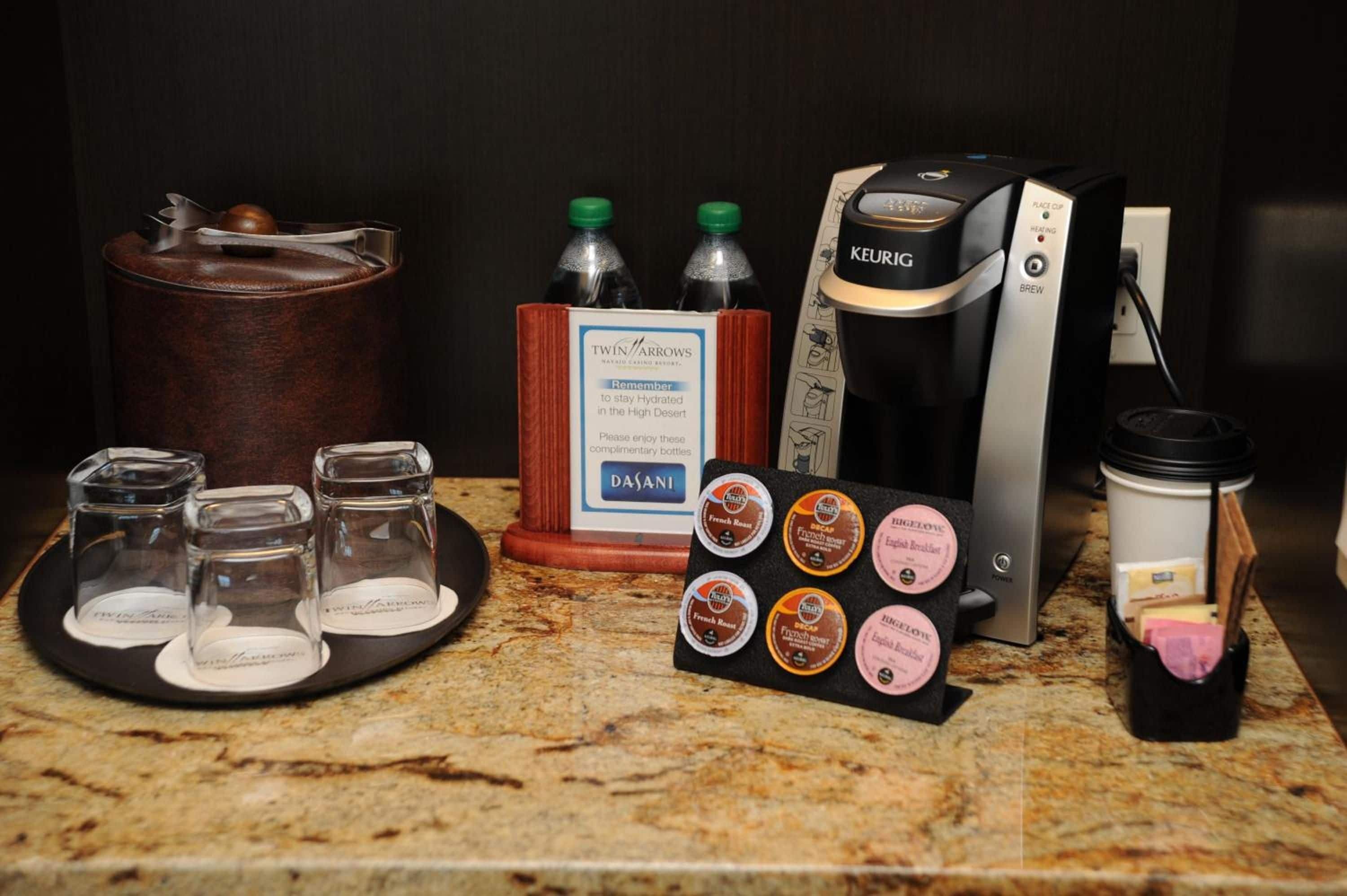 A coffee station with a Keurig coffee maker, a water dispenser, and a tray with coffee pods and glasses.