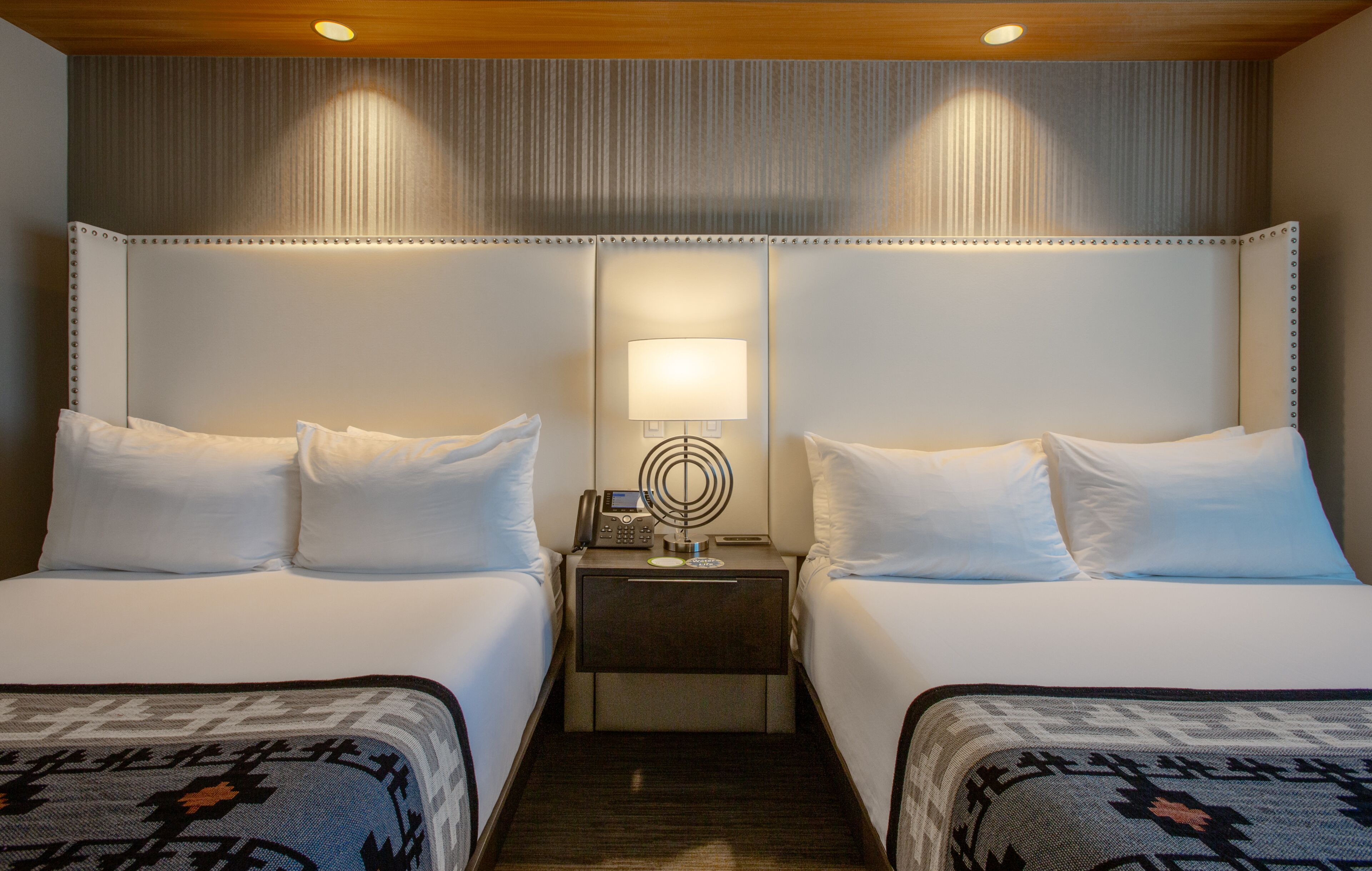 A hotel room with two beds, a nightstand with a lamp, and a patterned rug.