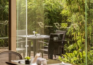 A dining area with wicker furniture and a glass partition, surrounded by lush greenery. - Fraser Suites Guangzhou (Guangzhou)