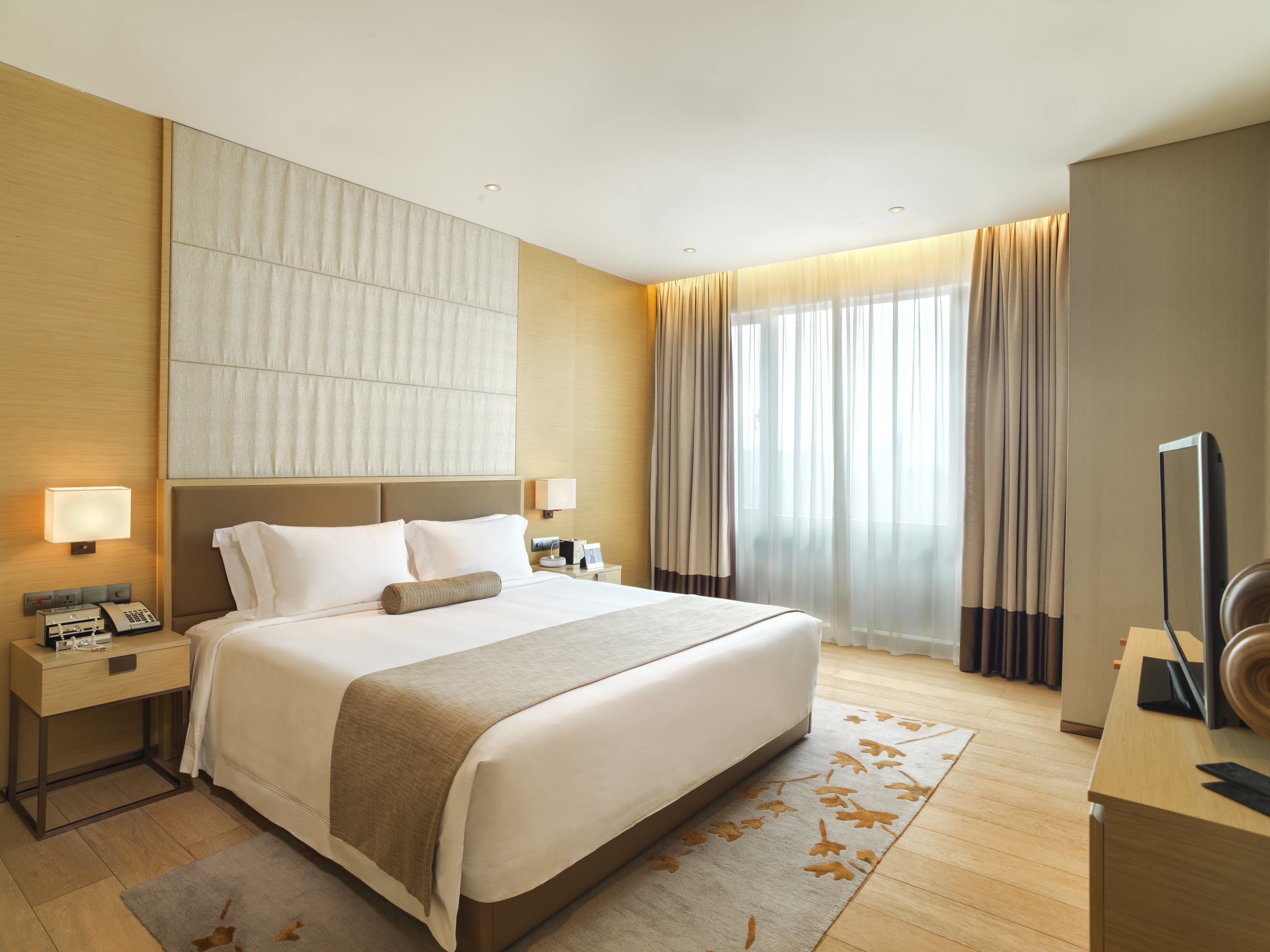 A hotel room with a large bed, bedside tables, a flat-screen TV, and a window with curtains.
