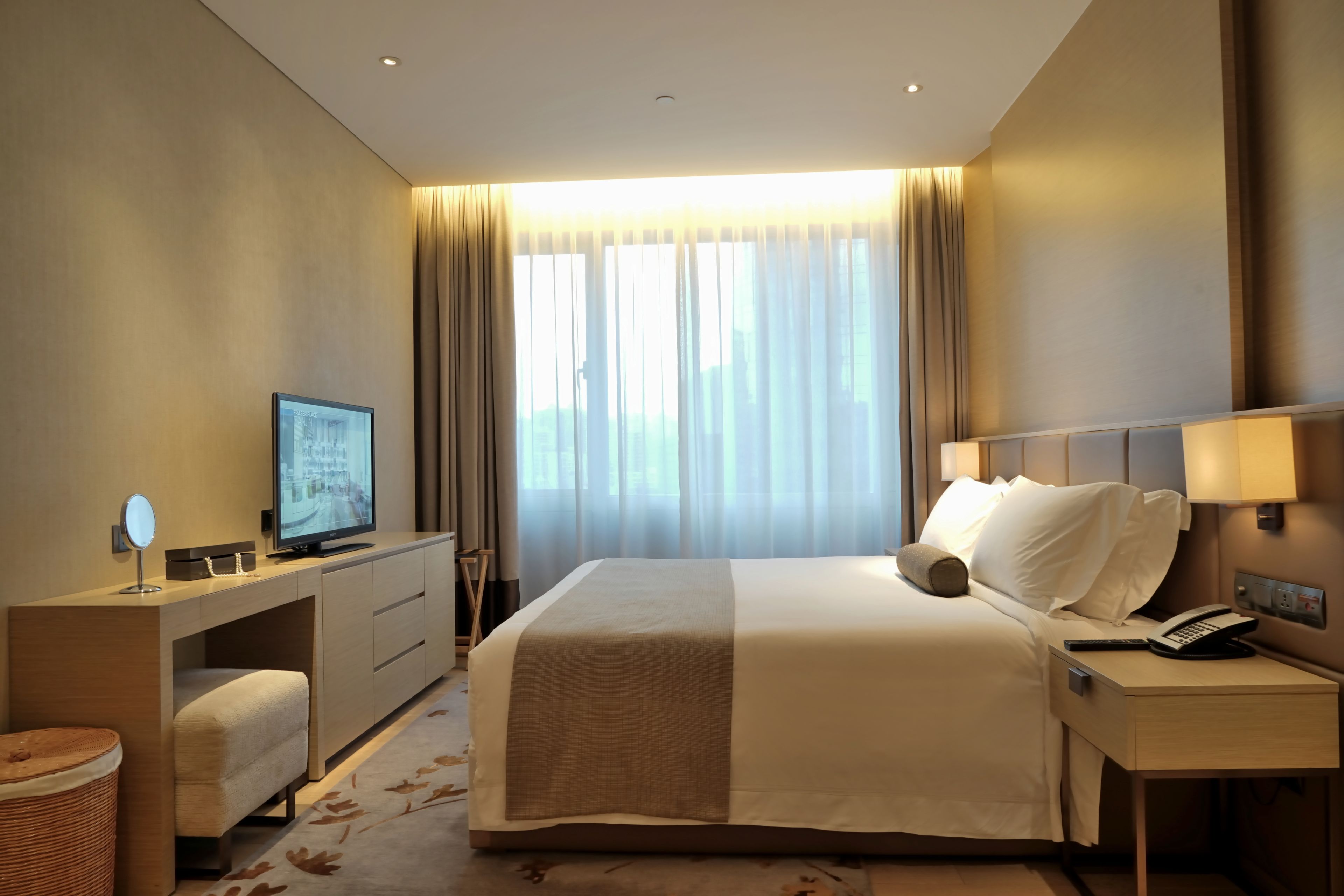 Habitación de hotel con cama, mesita de noche, lámpara, televisor, escritorio y vistas al exterior a través de la ventana.