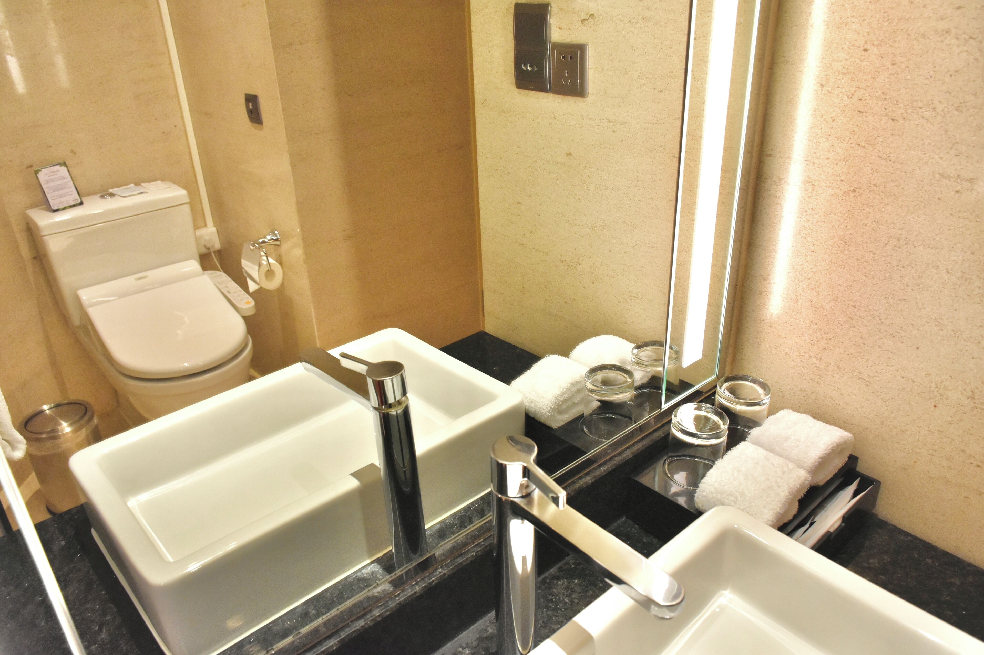 Un baño con inodoro, dos lavamanos, un espejo y un perchero para toallas.
