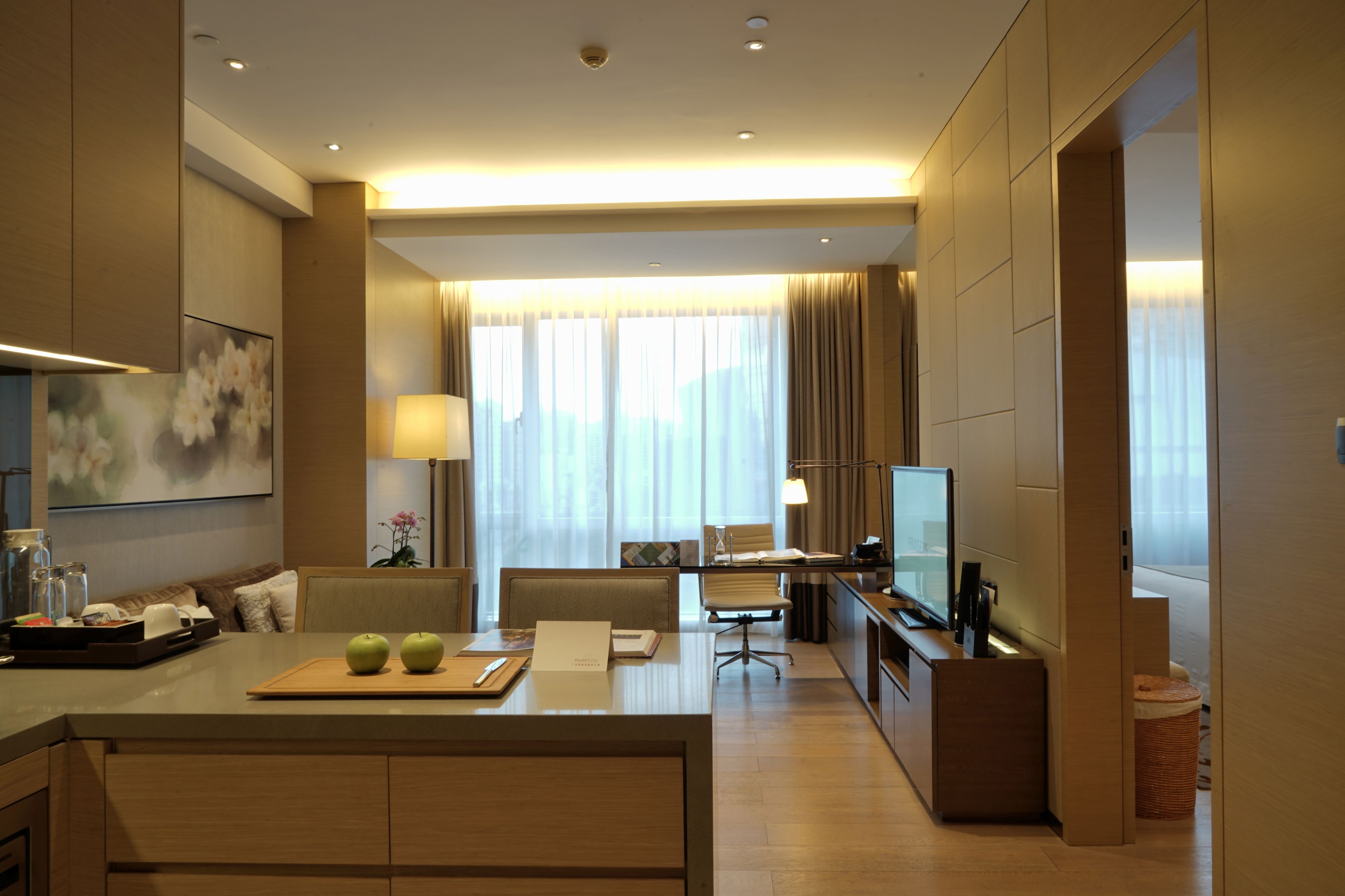 A modern hotel room with a dining area, a TV, and a large window with curtains.