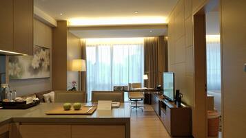 A modern hotel room with a dining area, a TV, and a large window with curtains.