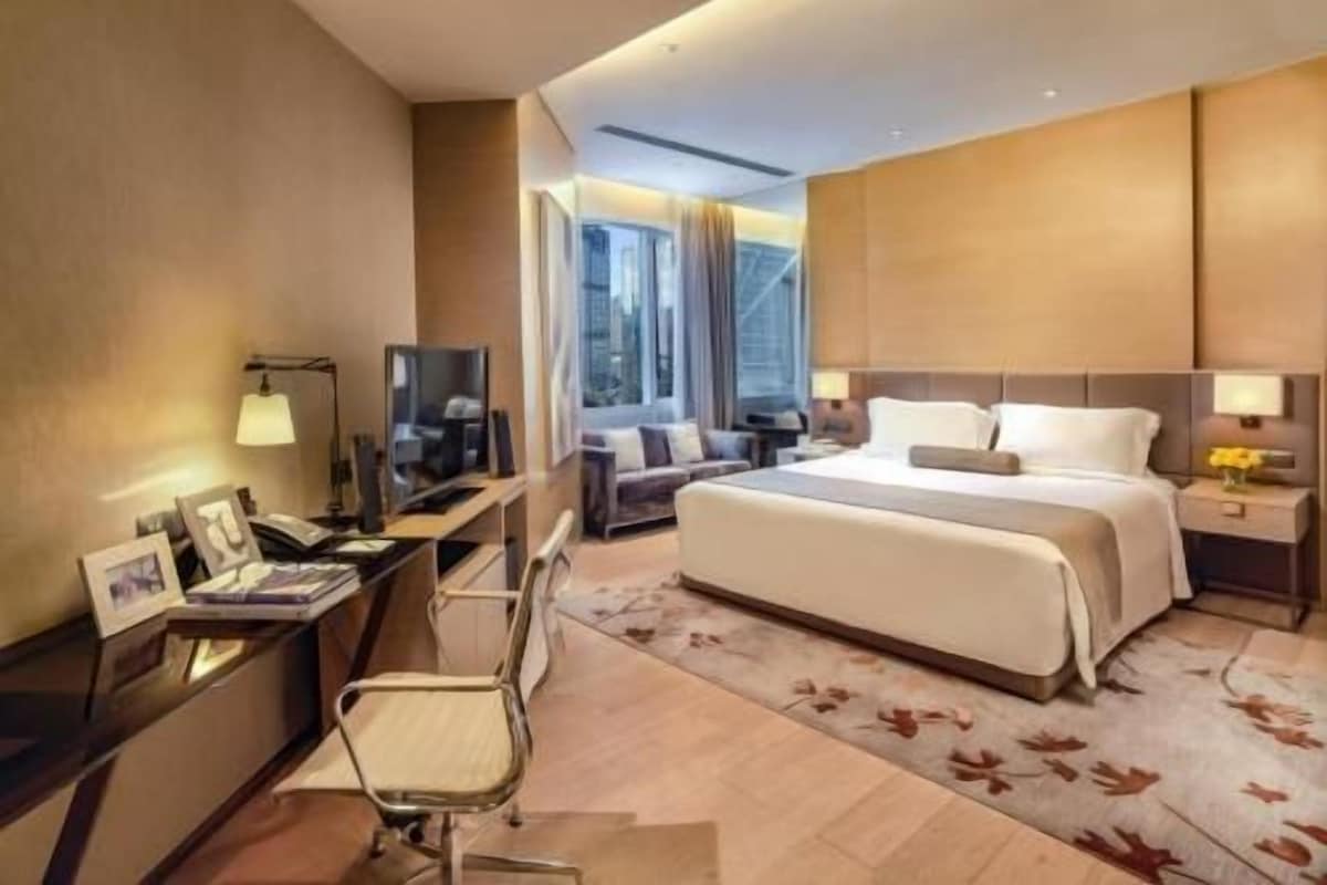Habitación de hotel con cama, escritorio, silla, televisor y vistas a la ciudad.