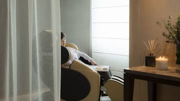 A person relaxing in a massage chair with a window view, a candle, and a diffuser on a table.