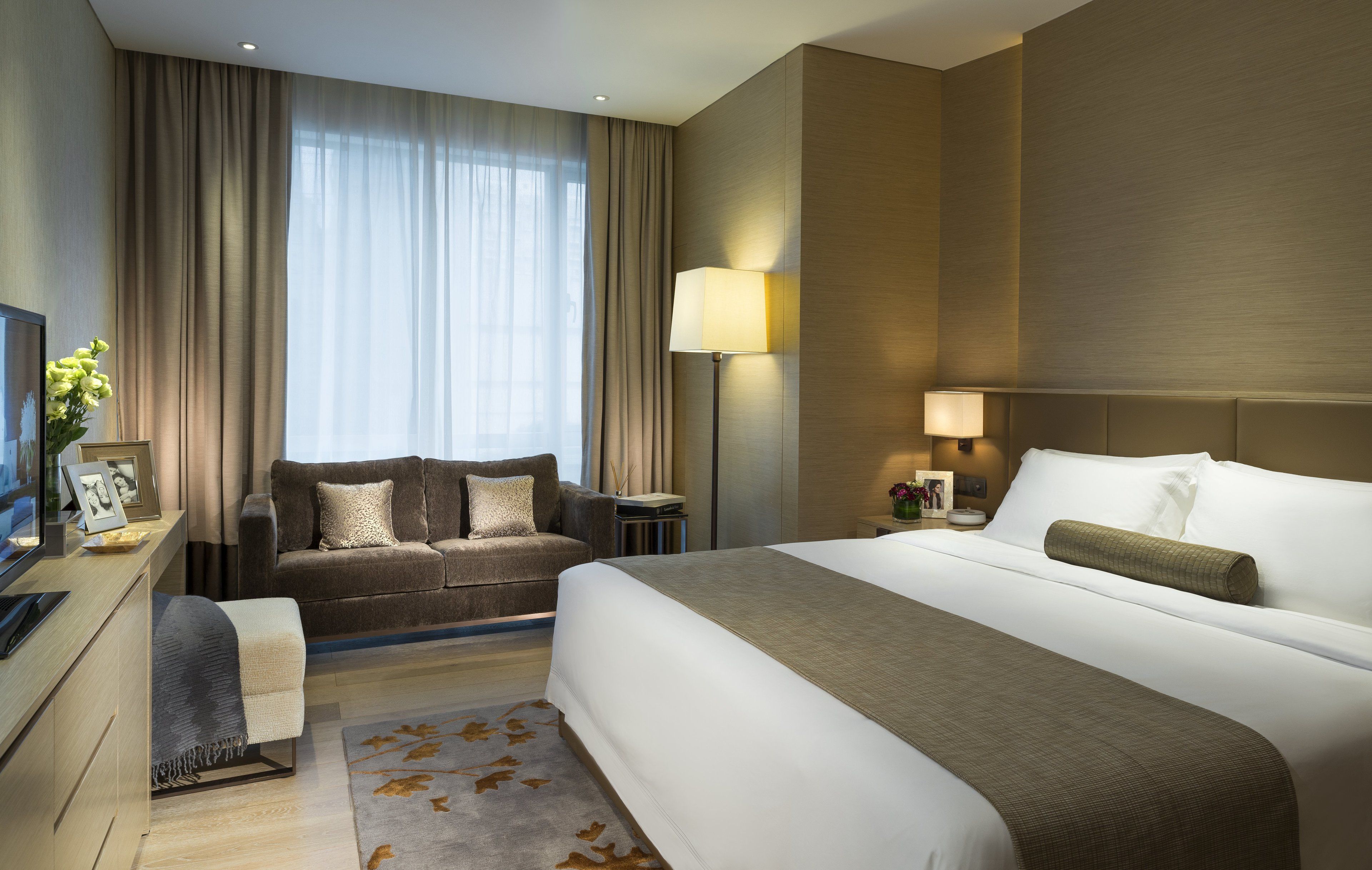 Habitación de hotel con una cama grande, un sofá, un escritorio con computadora, una lámpara y una ventana con cortinas.