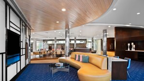 Un hall d’entrée moderne avec un plafond en bois incurvé, un canapé jaune agrémenté de coussins, une table basse et un tapis bleu à motifs.