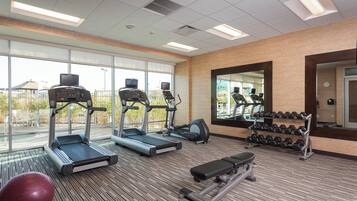 A gym with treadmills, an elliptical, a bench, dumbbells, and a red exercise ball.