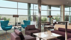 Un espace de détente moderne, doté de sièges confortables, de grandes fenêtres et offrant une vue sur l’extérieur.