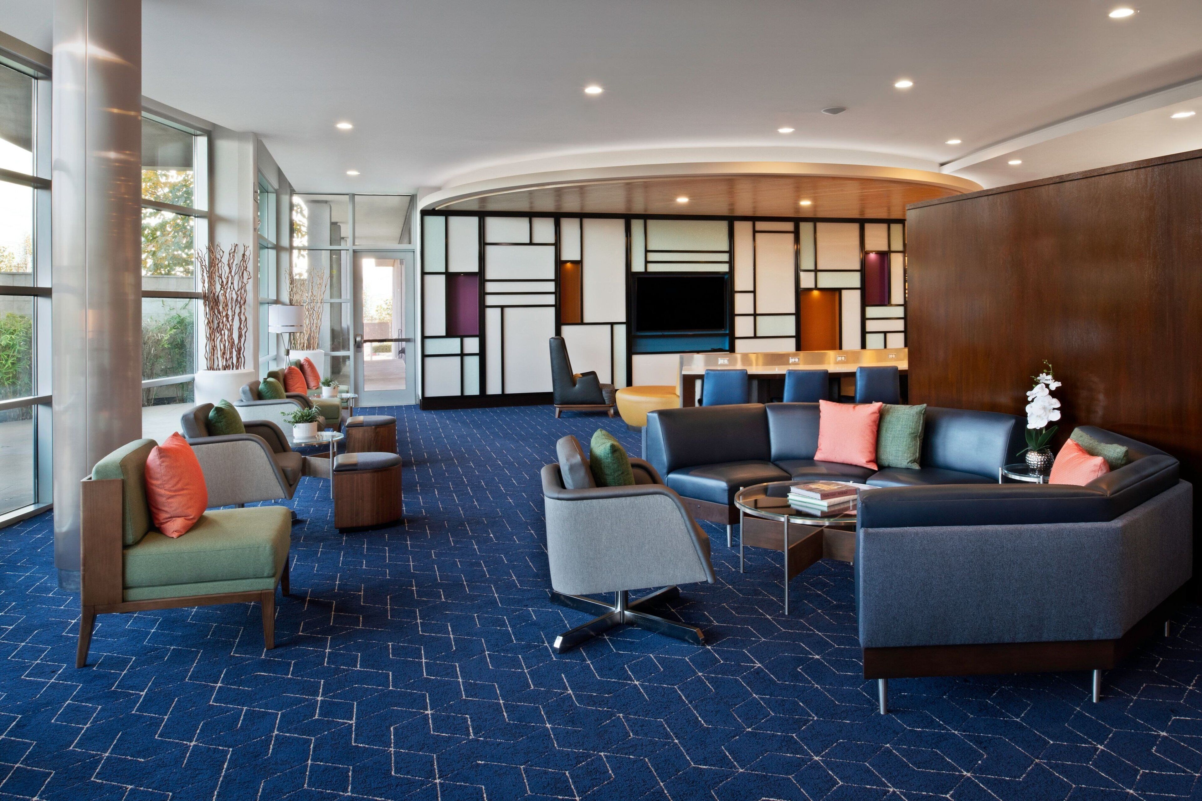 Een moderne hotellobby met een gebogen zithoek, een flatscreen-televisie en een groot raam met uitzicht op het omliggende landschap.
