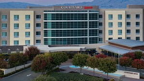 Un hôtel Courtyard Marriott doté d’une façade moderne en verre, de plusieurs étages et d’une cour aménagée avec des arbres et une piscine.
