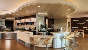 Un espace bar moderne doté d’un comptoir incurvé, d’appareils électroménagers en acier inoxydable et de tabourets de bar contemporains.