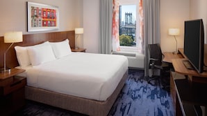 Une chambre d’hôtel avec un grand lit, un bureau avec un ordinateur, une télévision et une fenêtre avec des rideaux.