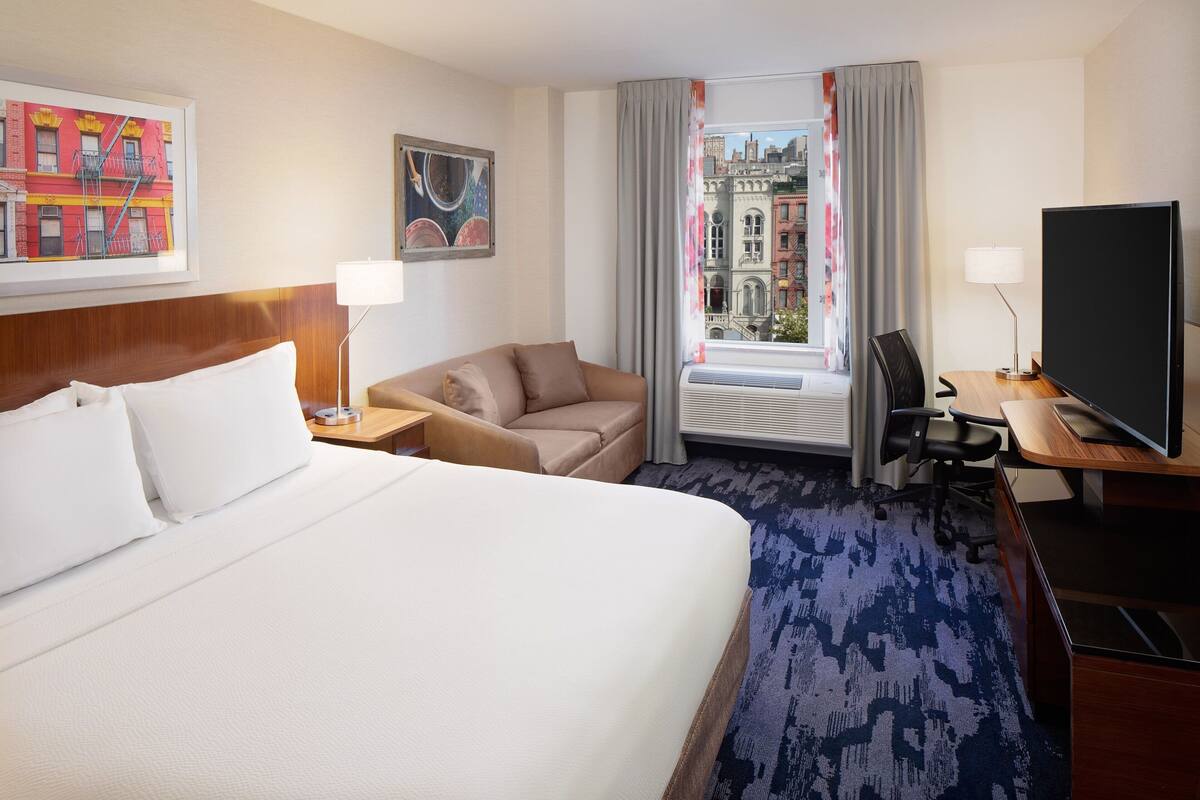 Ein Hotelzimmer mit einem großen Bett, einer Sitzecke, einem Schreibtisch mit Computer und einem Fernseher.