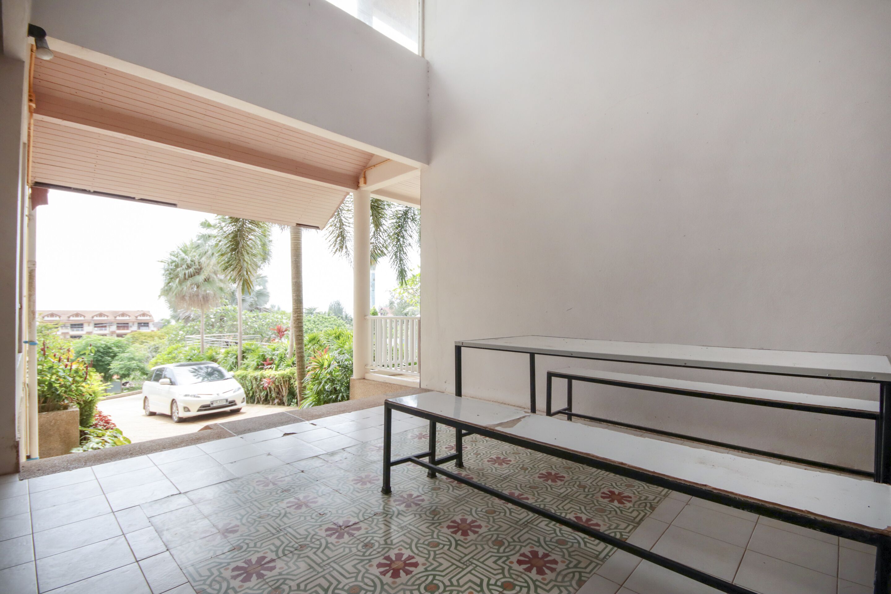 Habitación con balcón, un coche blanco estacionado fuera y suelo de baldosas.