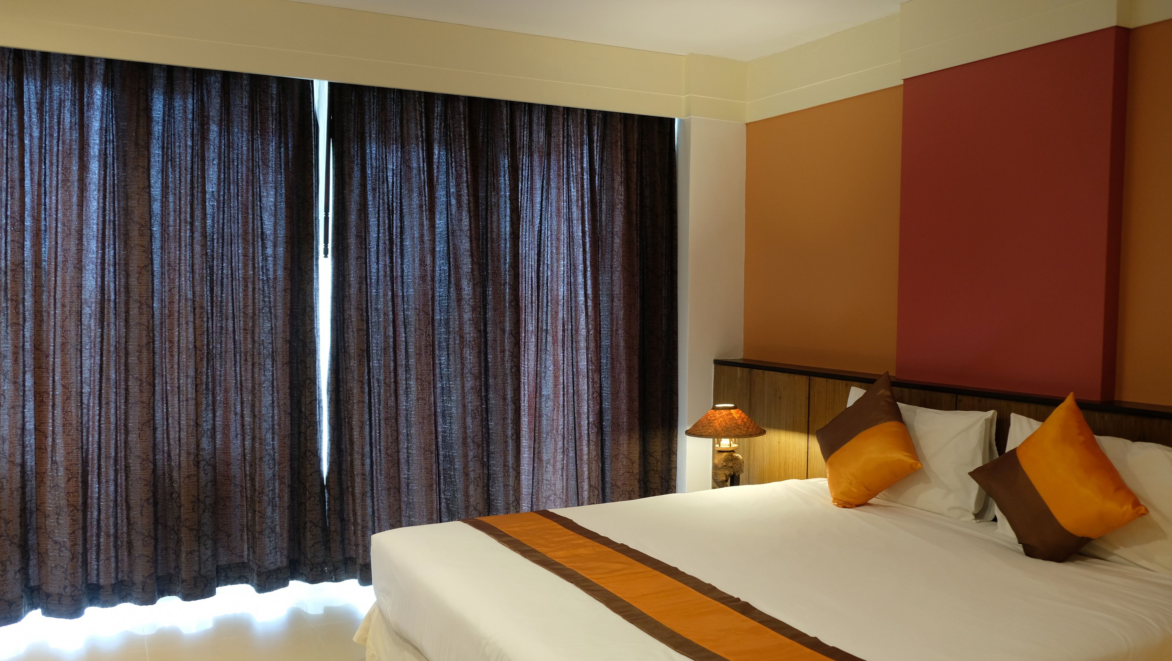 Una habitación de hotel con una cama grande, cortinas, una lámpara y una pared con un panel rojo.