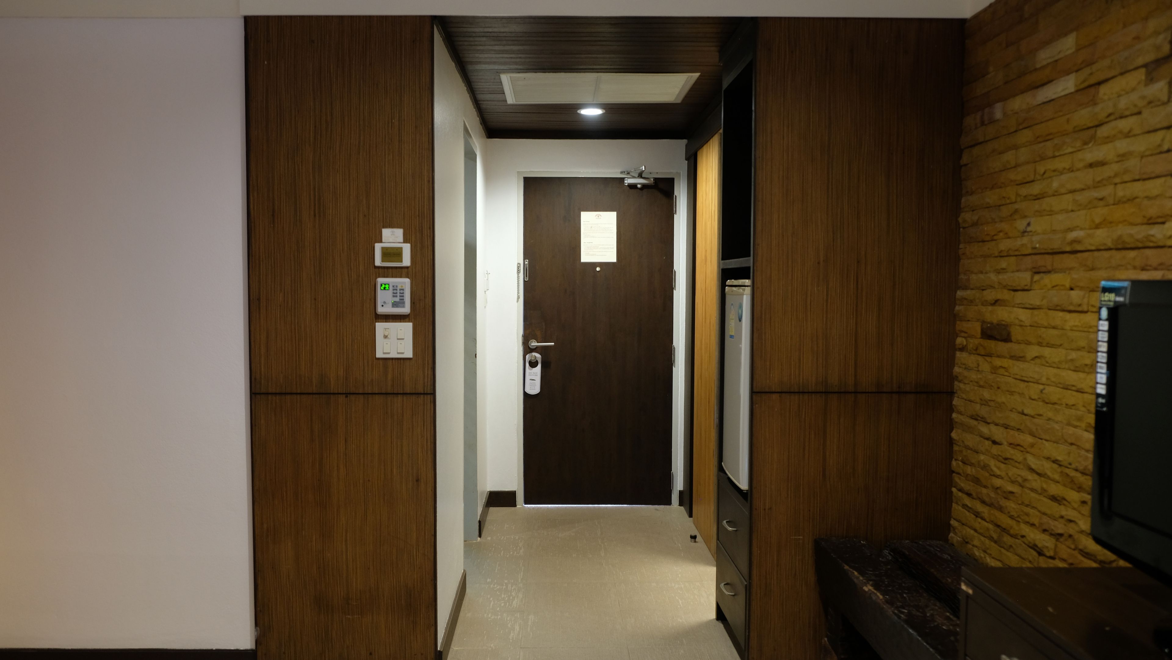 A hallway with a wooden door, a thermostat, and a refrigerator.
