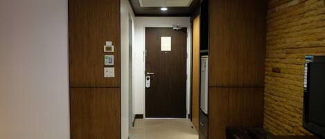 A hallway with a wooden door, a thermostat, and a refrigerator.