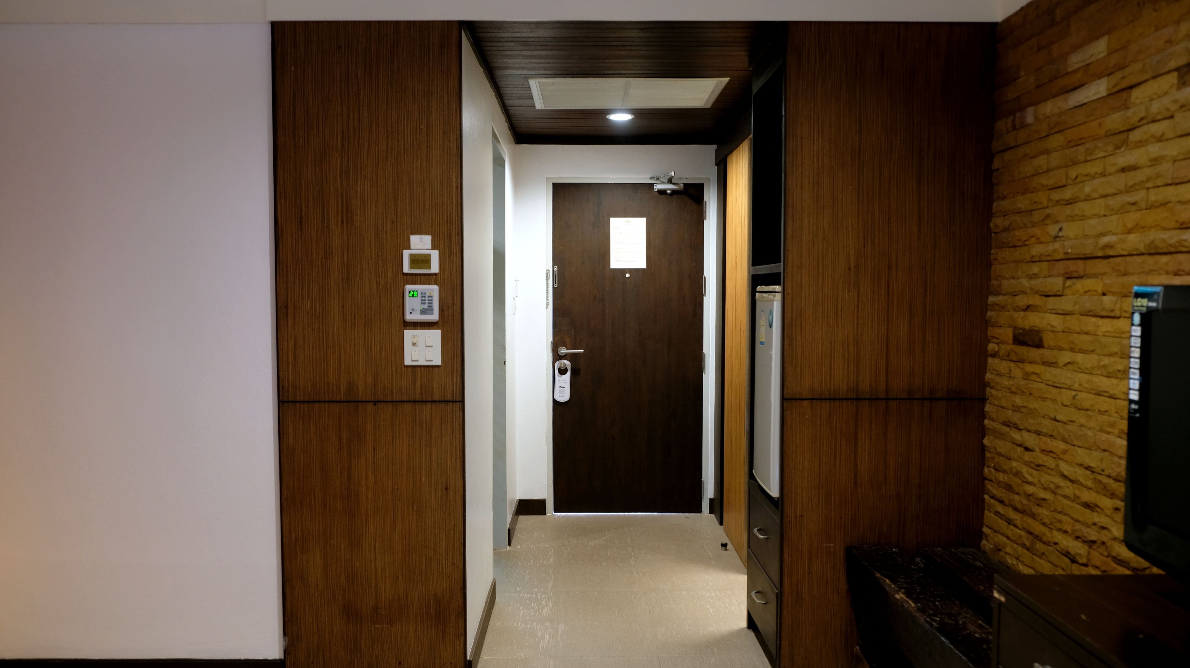 A hallway with wooden paneling, a door with a security lock, a thermostat, and a wall-mounted television.