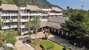 Ein mehrstöckiges Hotel mit Balkonen, umgeben von üppiger Vegetation und einer Bergkulisse.