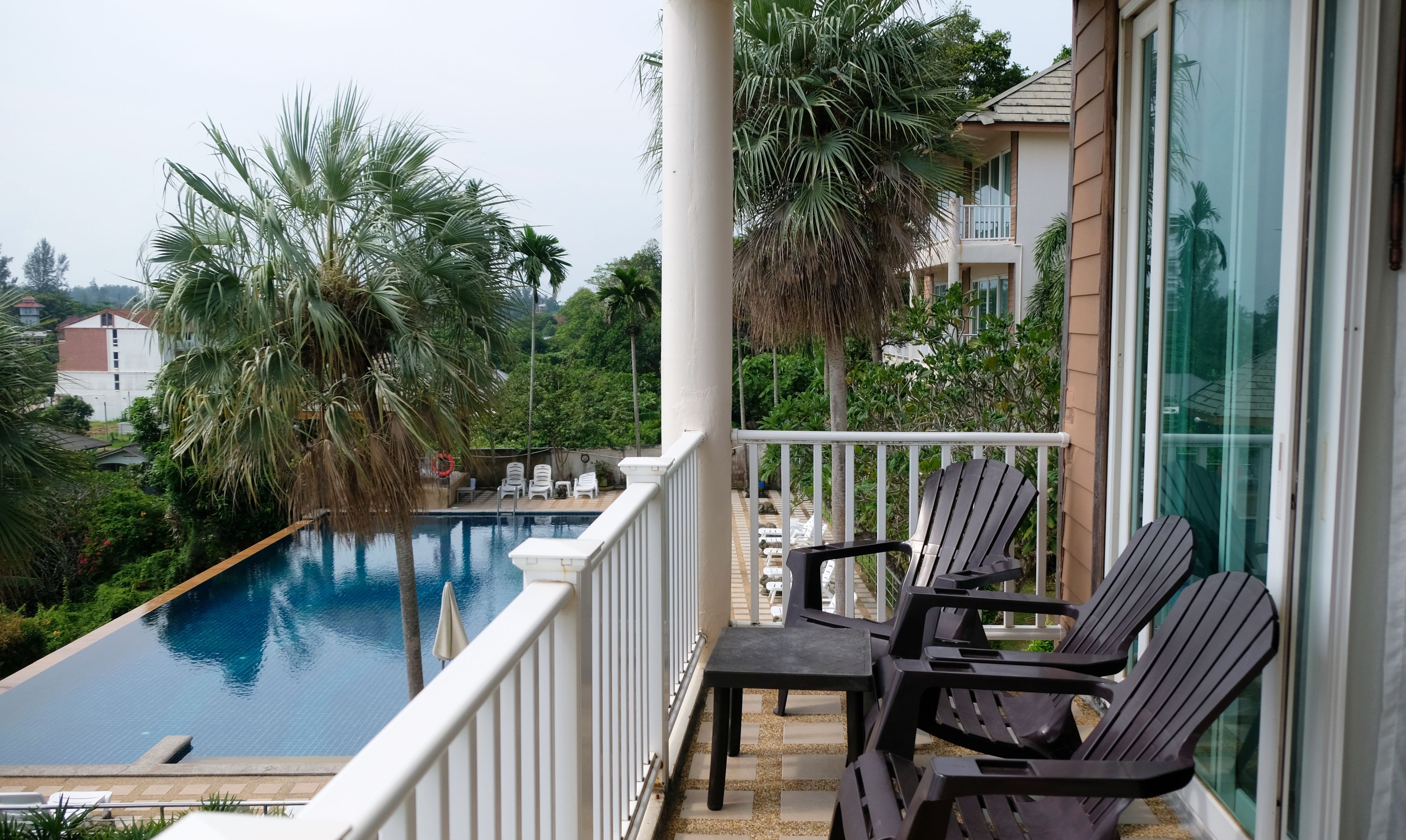 A balcony with a pool, lounge chairs, and a view of a residential area.